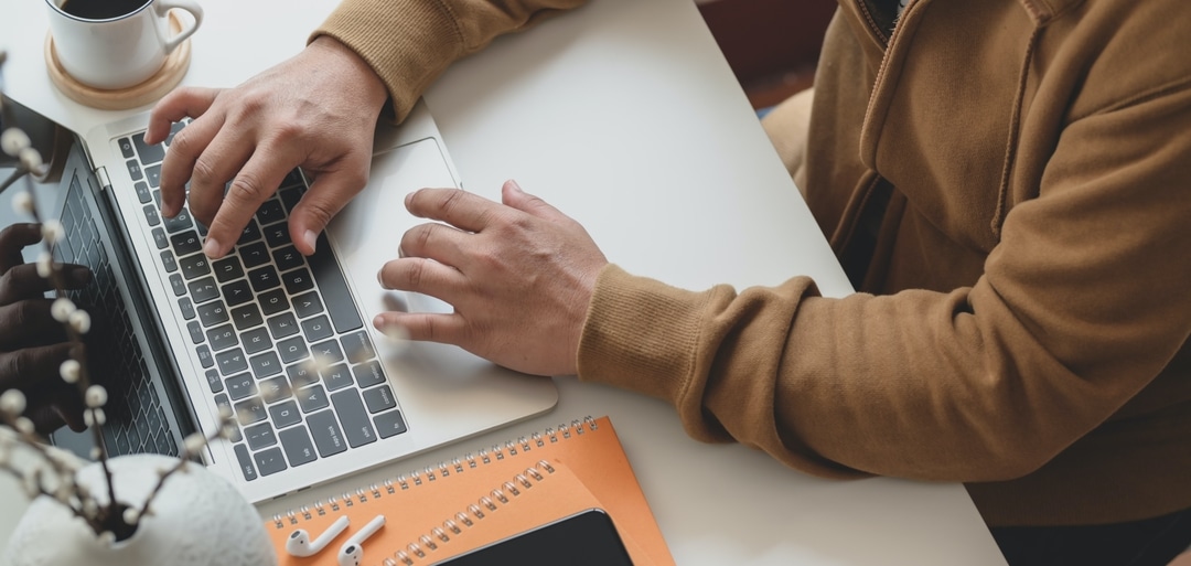 A person reviewing information on a laptop with a notebook and coffee