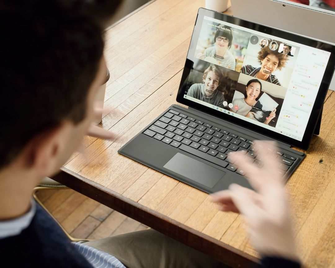 A person on a video call with team members shown on the laptop screen