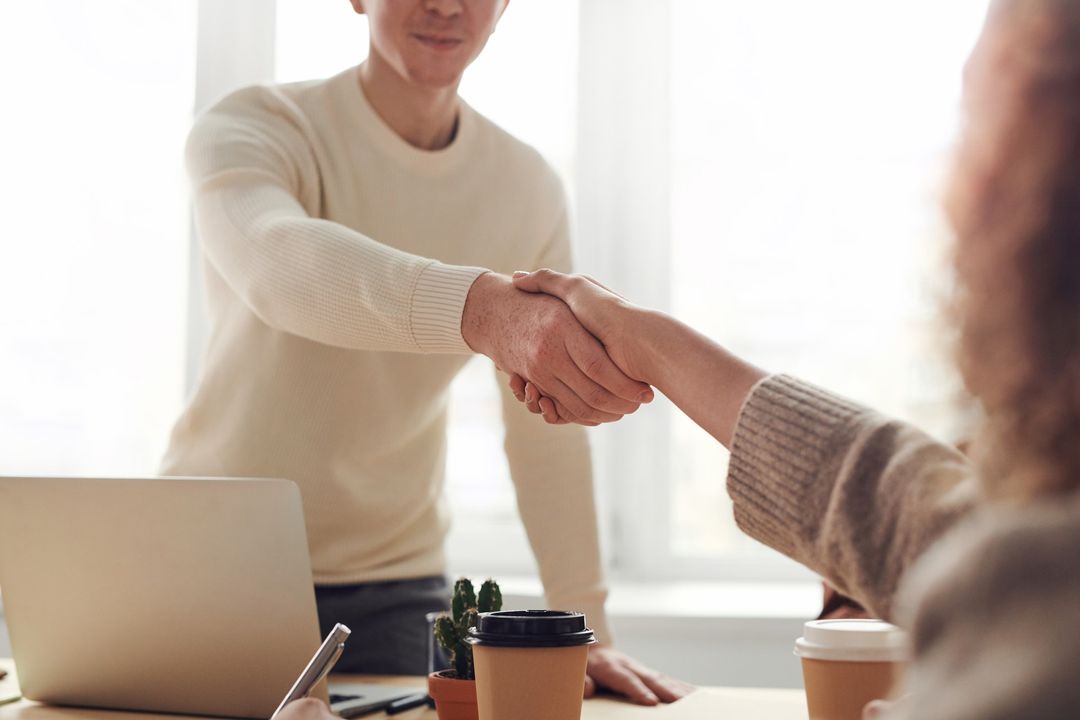 Two colleagues shaking hands across a desk in a welcoming meeting