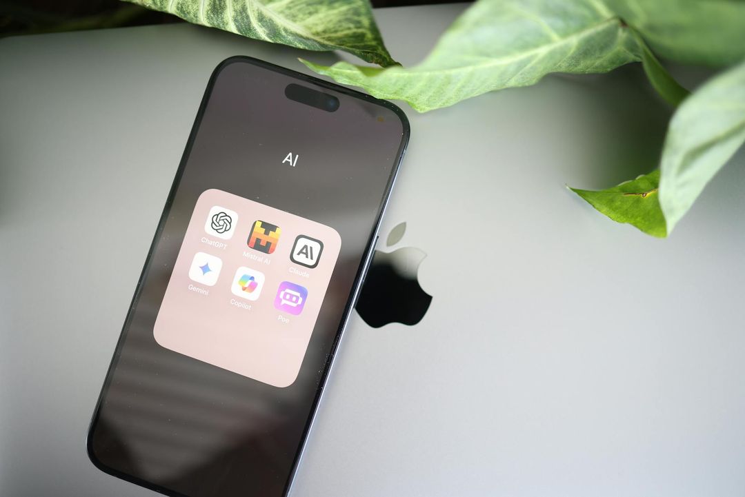 A smartphone showing a folder of AI apps beside a laptop