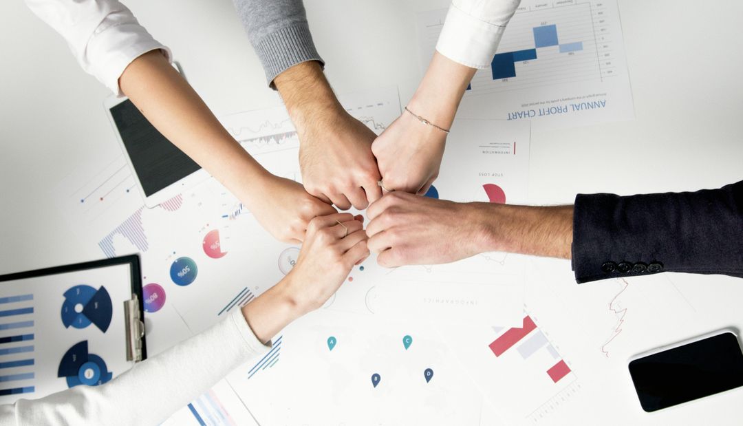 A team joining hands together over business charts on a desk